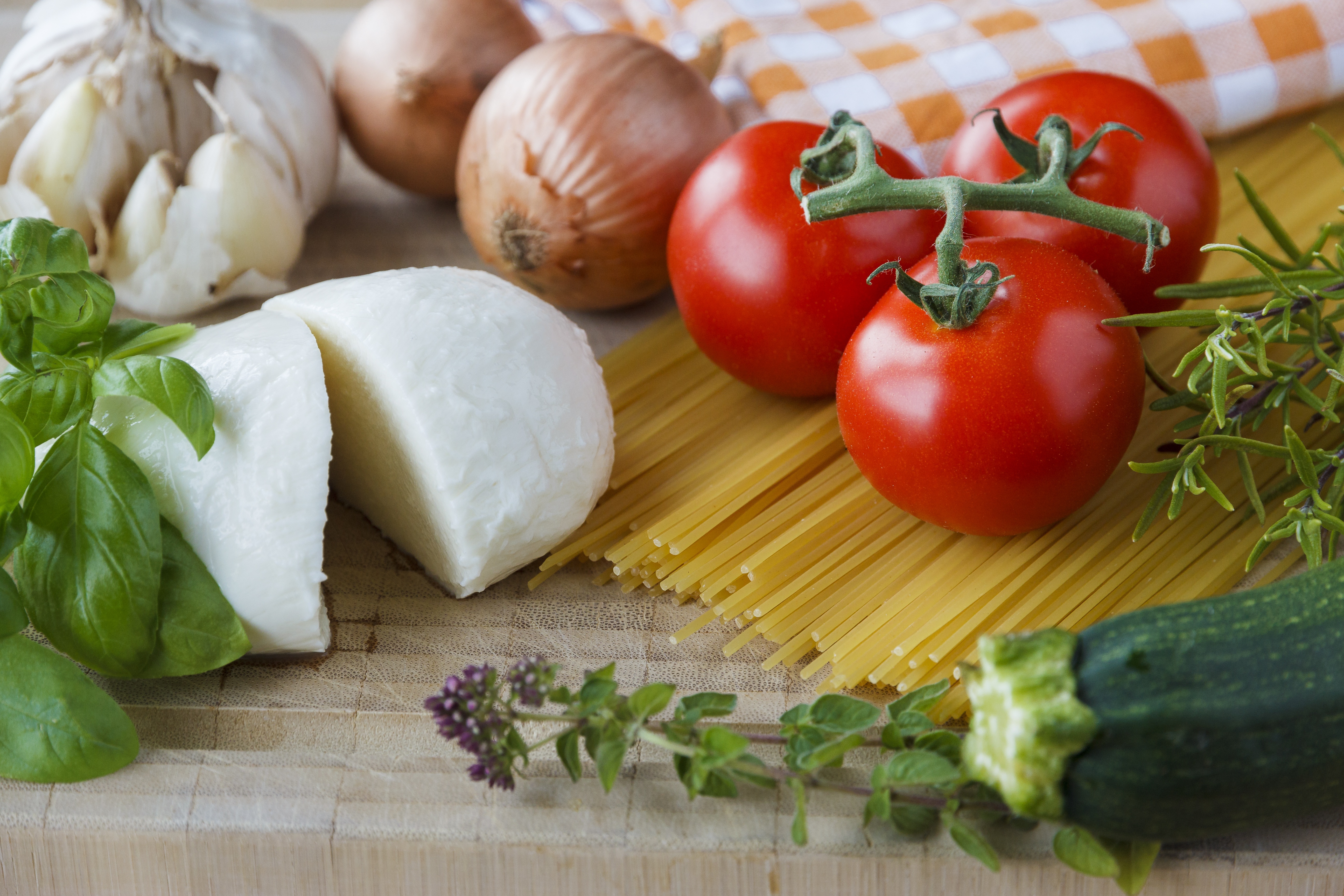 Some garlic, onion, tomato, vegetables, and pasta on a table